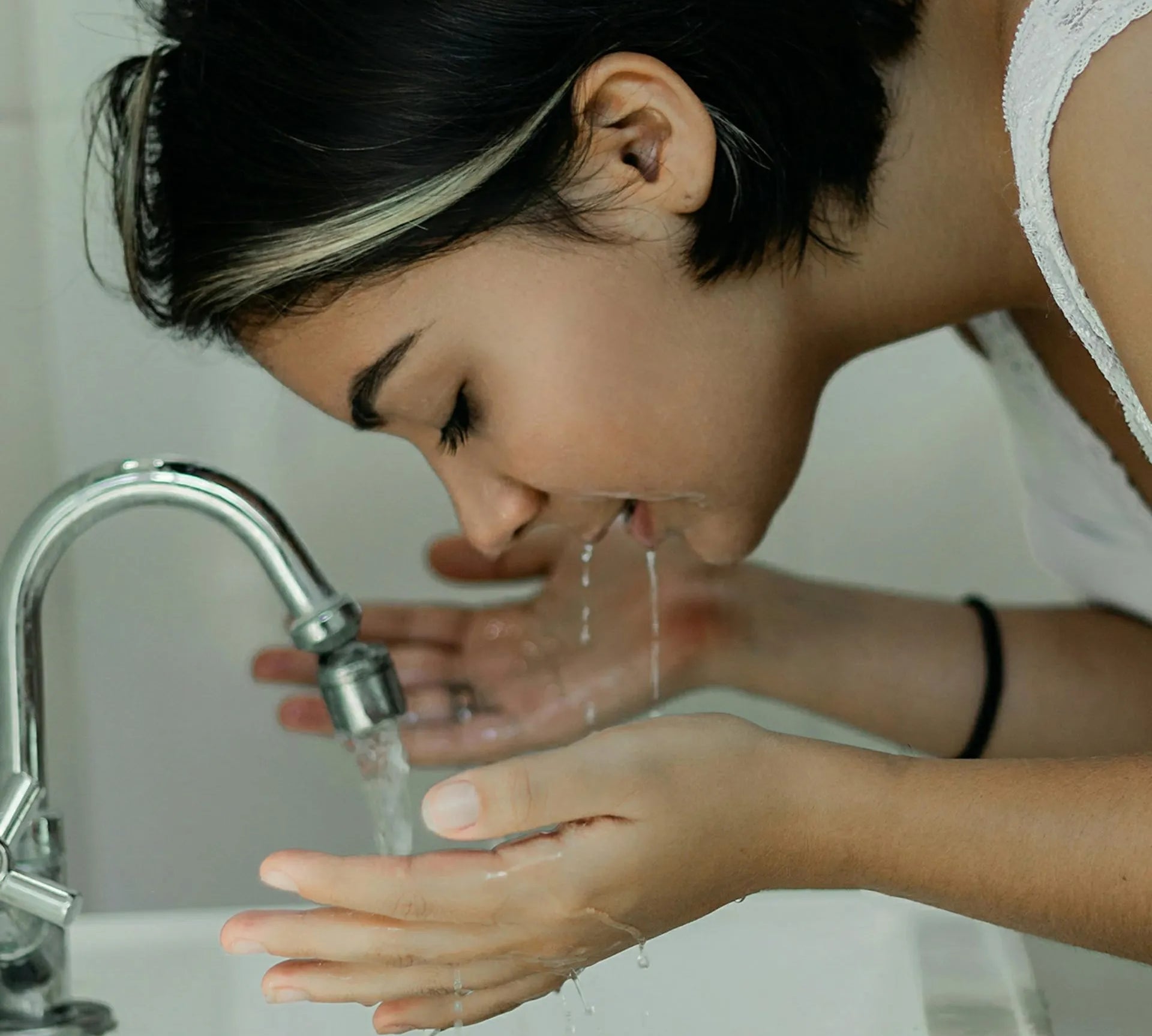 Woman rinsing her face at a sink