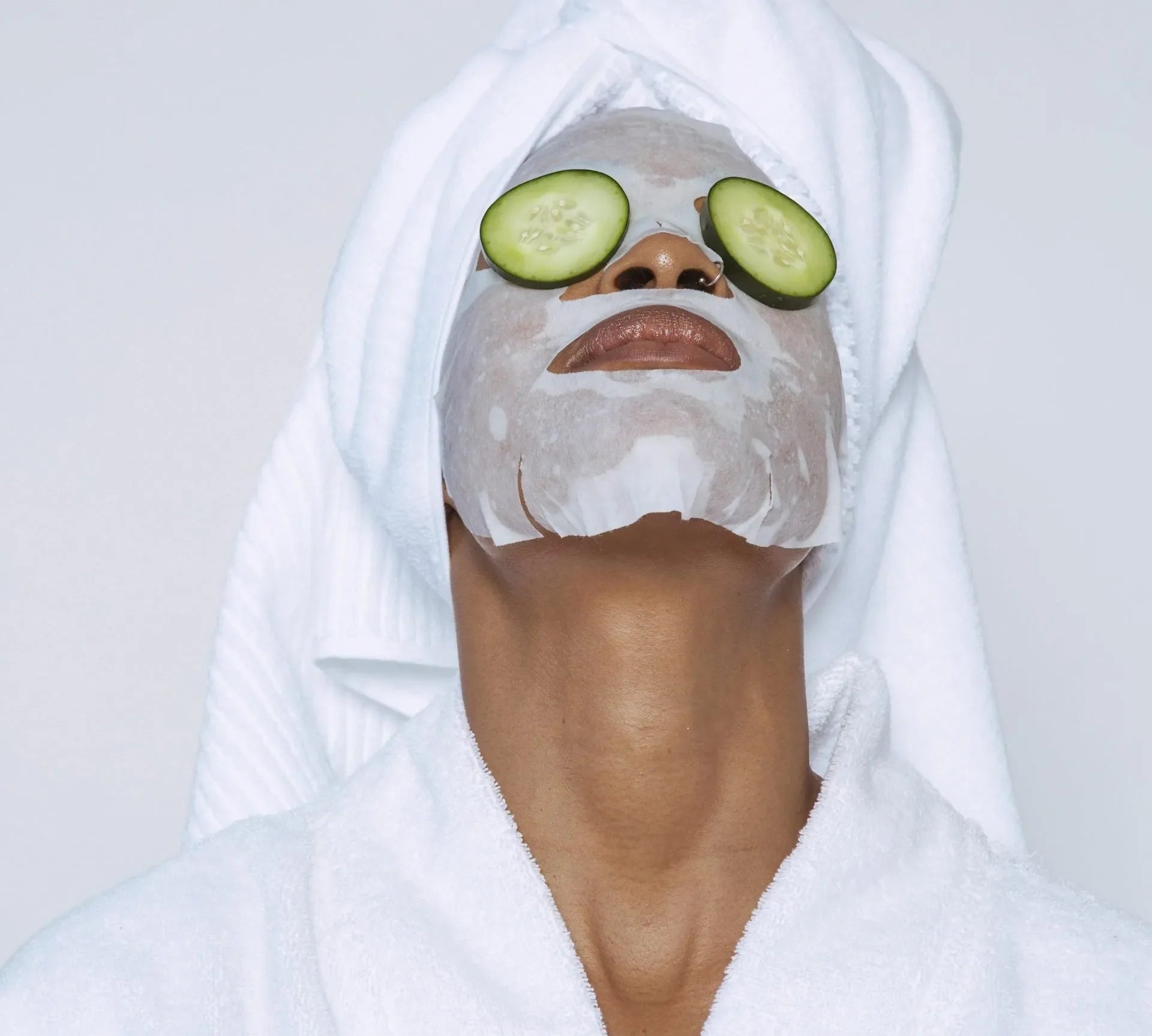 Woman in a robe and towel wrap with a sheet mask and cucumber slices on her eyes