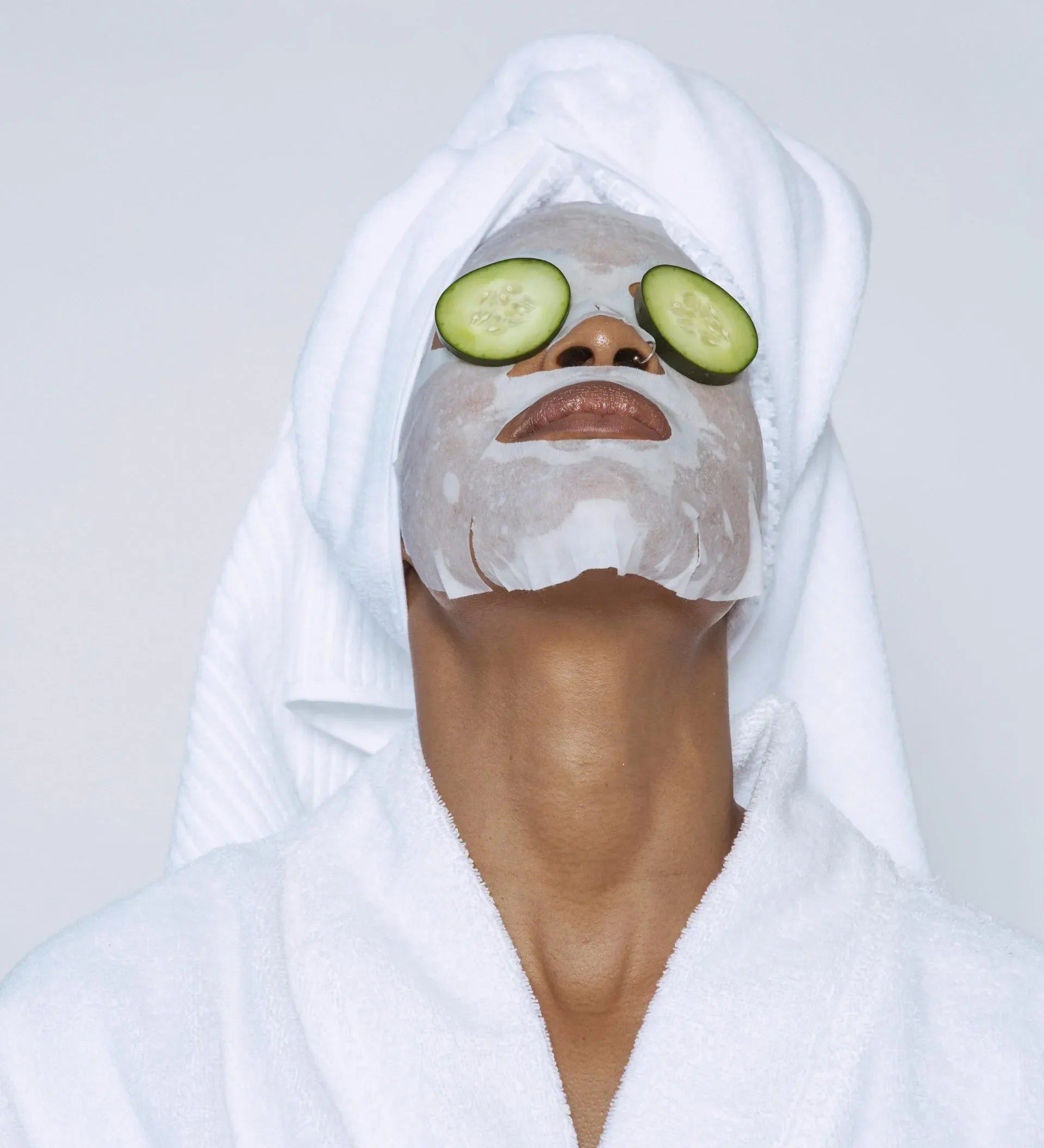 Woman in a robe and towel wrap with a sheet mask and cucumber slices on her eyes
