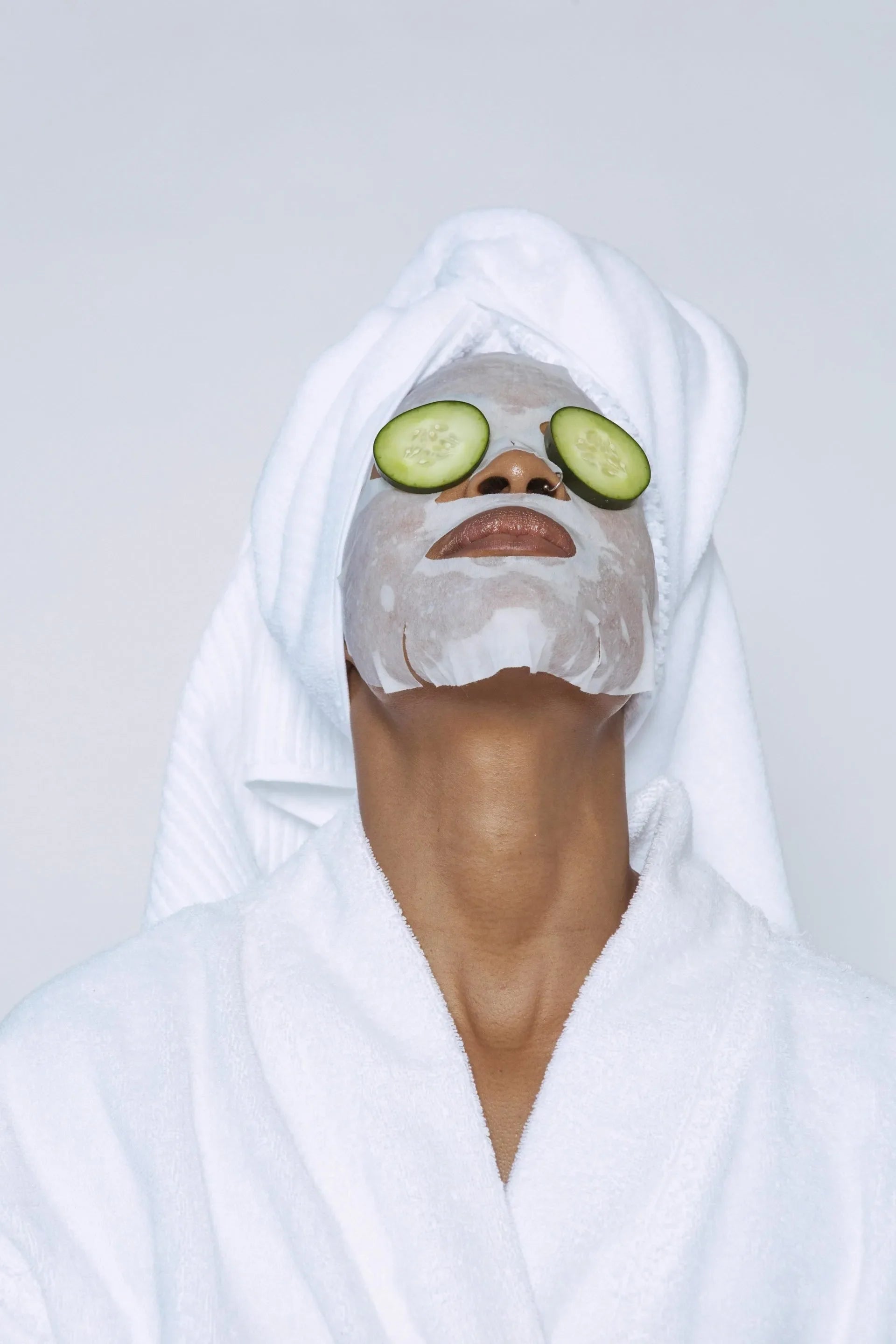 Woman in a robe and towel wrap with a sheet mask and cucumber slices on her eyes