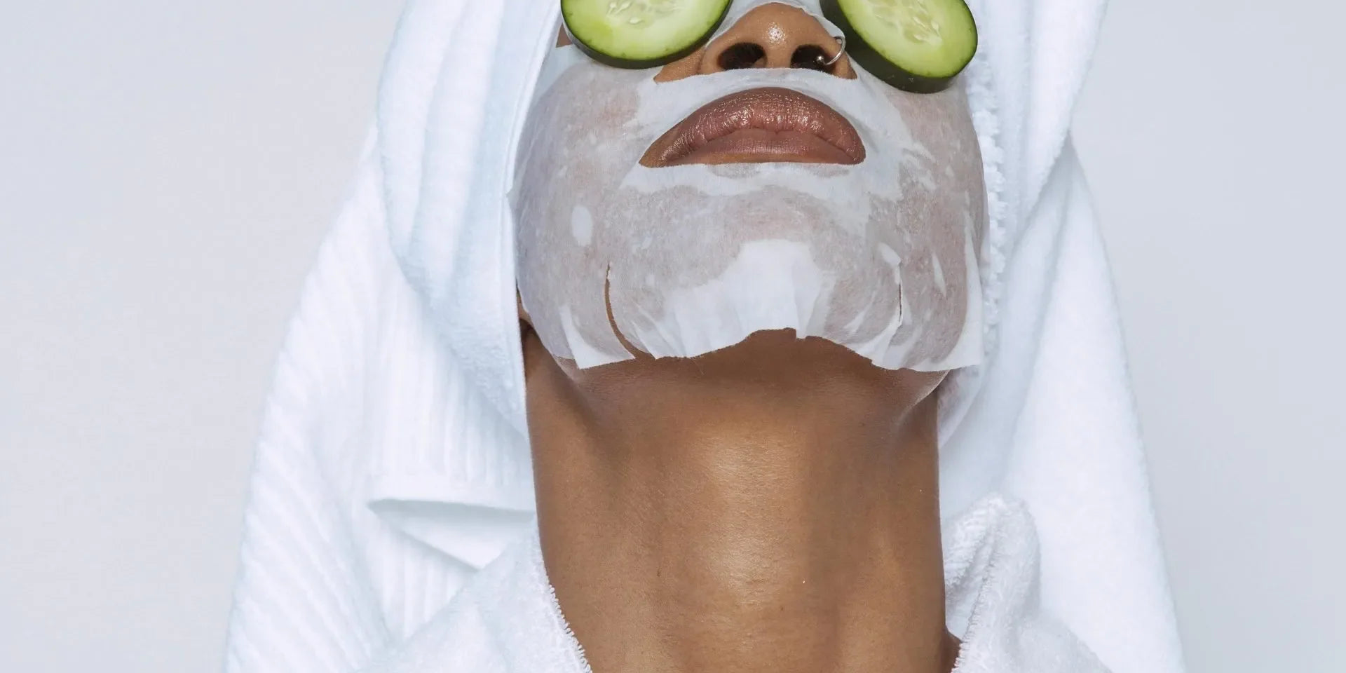Woman in a robe and towel wrap with a sheet mask and cucumber slices on her eyes