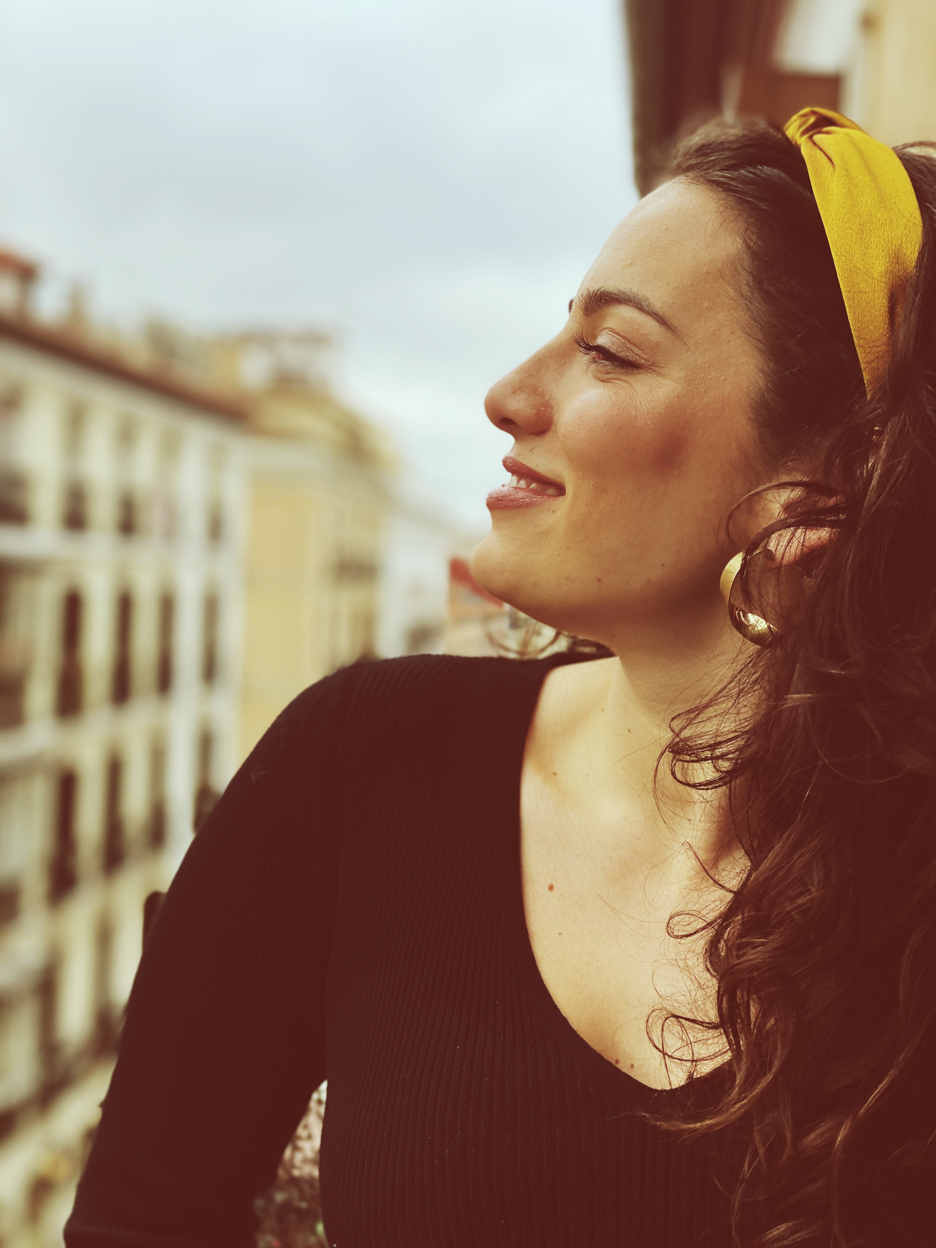 Woman in profile on a sunlit balcony with a yellow headband